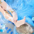 photo - 这是一张经过精心布景的Cosplay局部特写照片。画面中心是一位女性角色的双腿和双足，皮肤白皙，脚趾涂有淡粉色的指甲油。

角色腿上缠绕着白色的丝带，丝带上装饰